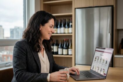 Femme en blazer regardant son ordinateur portable avec des bouteilles de vin en arrière-plan