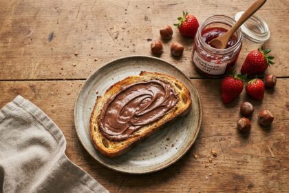 Vue de dessus d'une table petit déjeuner rustique avec tartine de pâte à tartiner et pot de confiture de fraises maison