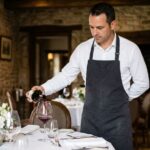 Sommelier versant un grand bourgogne rouge dans un verre en cristal lors d'un dîner gastronomique élégant